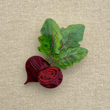 Load image into Gallery viewer, Acrylic brooch of a beet and green leaves on a textured beige background