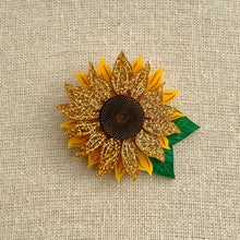 Load image into Gallery viewer, Acrylic sunflower brooch with gold petals and green leaf on a textured beige background