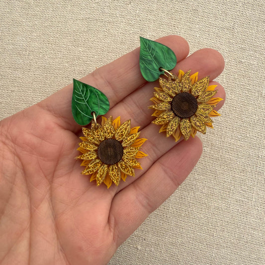 Sunflower earrings held in a hand against a beige background
