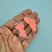 Load image into Gallery viewer, Hand holding pink wing-shaped earrings against a light blue background

