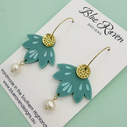 Green leaf-shaped earrings with gold accents and pearl details on a Blue Raven Designs card.