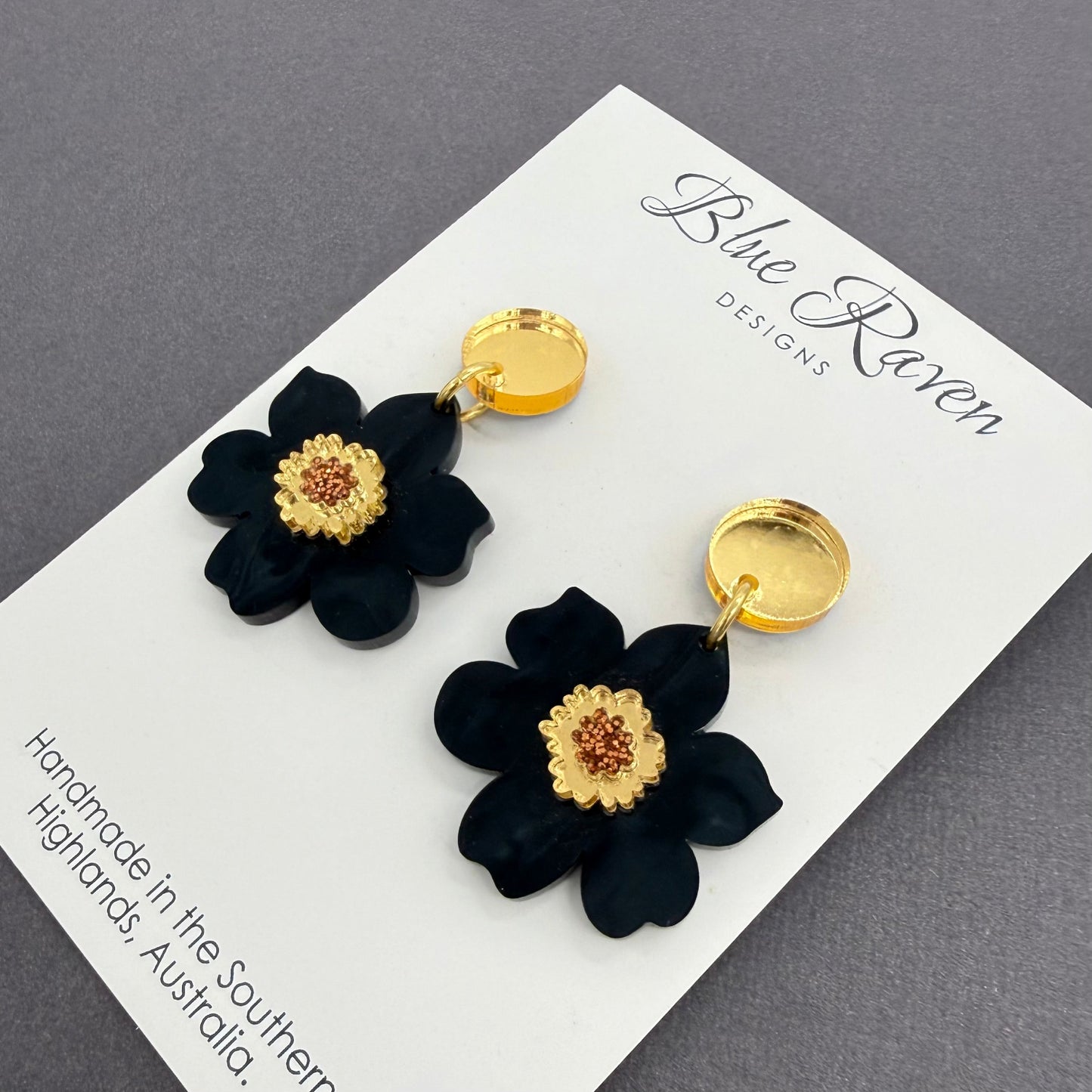 Black flower earrings with gold centers on a Blue Raven Designs card.