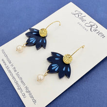 Load image into Gallery viewer, Pair of blue flower-shaped earrings with gold accents on a Blue Raven Designs card.
