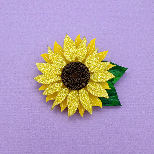 Yellow acrylic sunflower brooch with a green leaf on a purple background