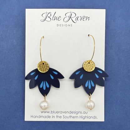 Pair of blue flower-shaped earrings with gold centers and pearl drops on a Blue Raven Designs card against a blue background.