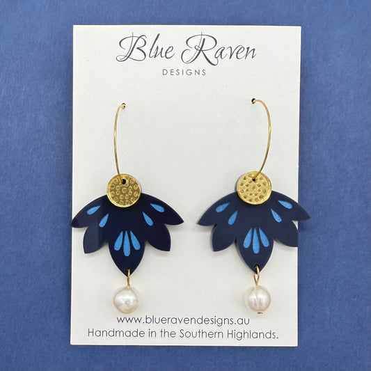 Pair of blue flower-shaped earrings with gold centers and pearl drops on a Blue Raven Designs card against a blue background.