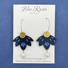 Load image into Gallery viewer, Pair of blue flower-shaped earrings with gold centers and pearl drops on a Blue Raven Designs card against a blue background.
