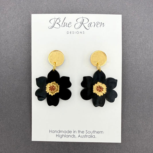 Black flower earrings with gold centers on a Blue Raven Designs card against a gray background