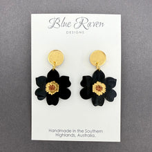 Load image into Gallery viewer, Black flower earrings with gold centers on a Blue Raven Designs card against a gray background
