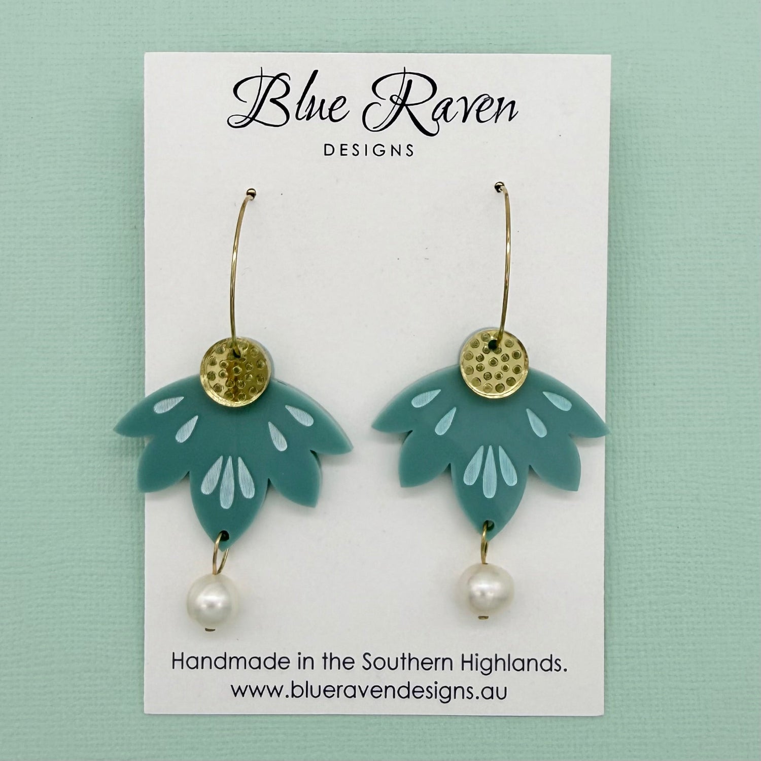 Teal earrings with gold and pearl details on a Blue Raven Designs card against a light green background.