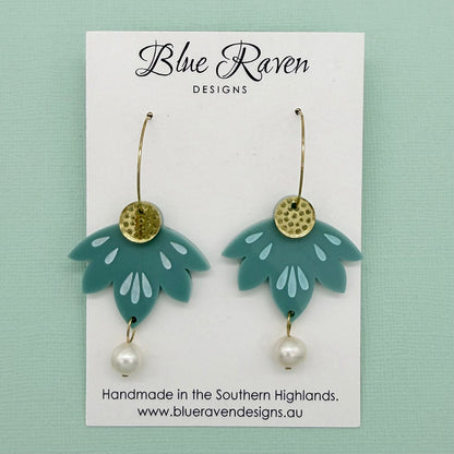 Teal earrings with gold and pearl details on a Blue Raven Designs card against a light green background.
