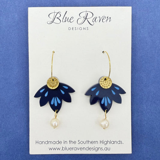 Pair of blue flower-shaped earrings with gold accents on a Blue Raven Designs card.