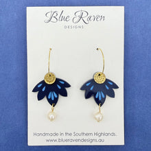 Load image into Gallery viewer, Pair of blue flower-shaped earrings with gold accents on a Blue Raven Designs card.
