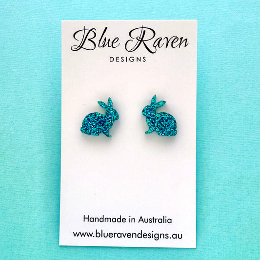 Blue glitter bunny earrings on a Blue Raven Designs card against a light blue background