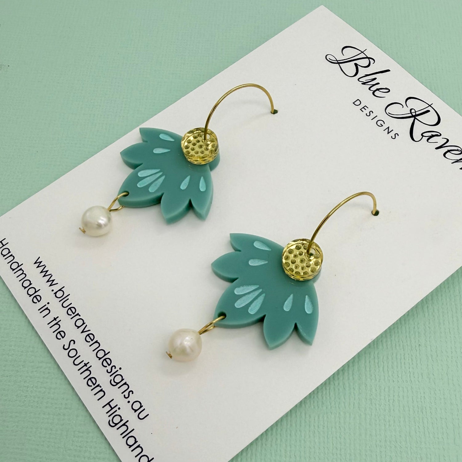Green leaf-shaped earrings with pearl details on a Blue River Designs card.
