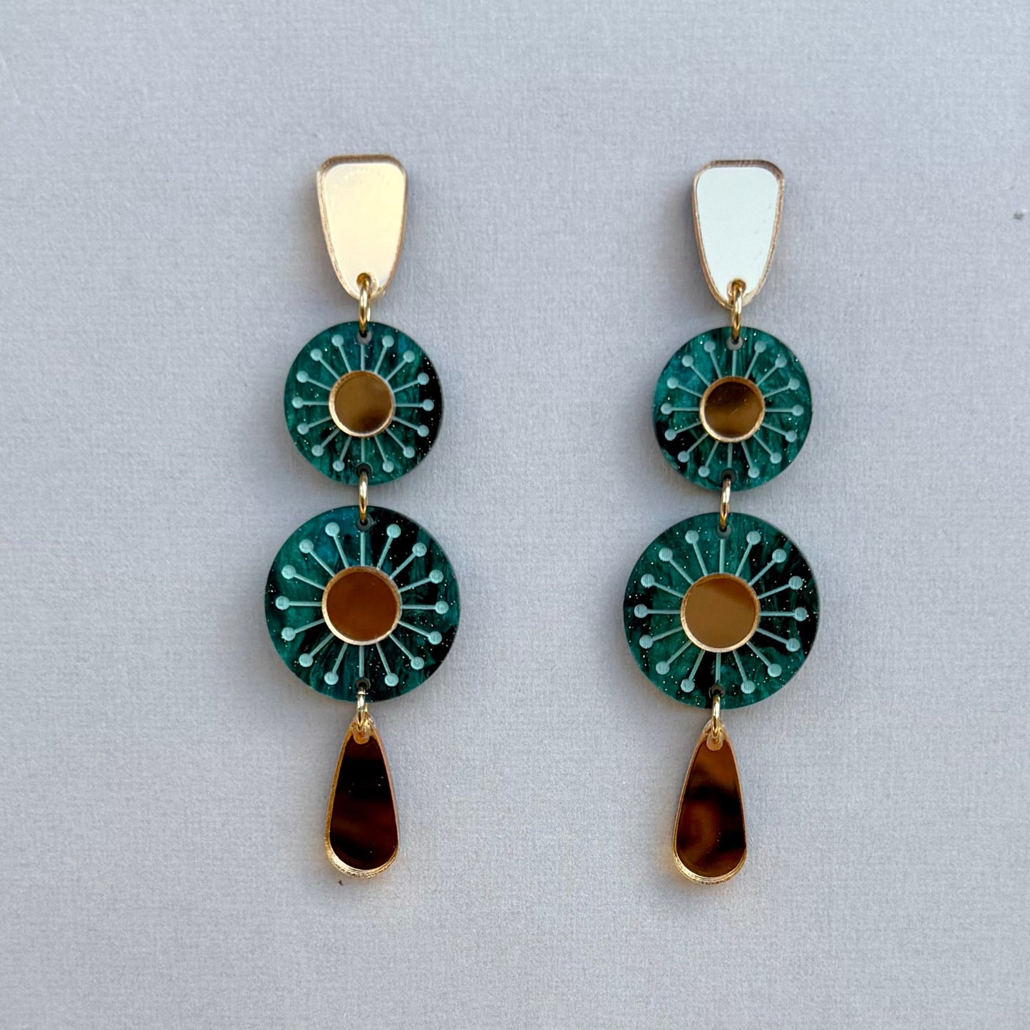 Pair of earrings with green circular designs and gold accents on a light gray background