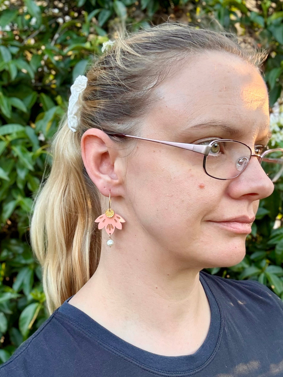 Woman wearing glasses and a floral earring with a blurred green background