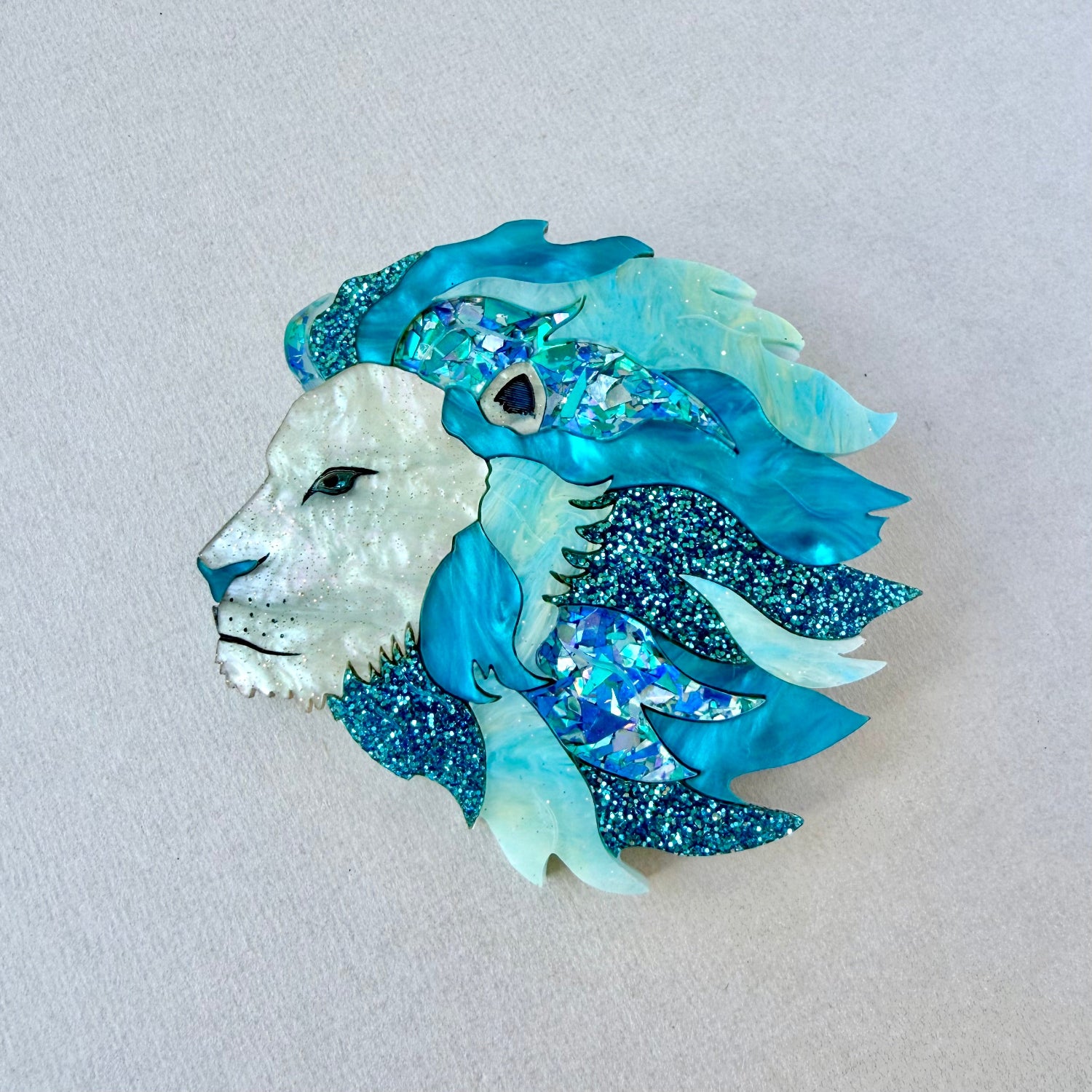Decorative brooch with a lion design in blue and white on a light gray background