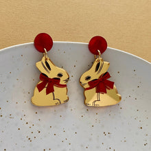 Load image into Gallery viewer, Gold bunny earrings with red bows on a white plate against a beige background
