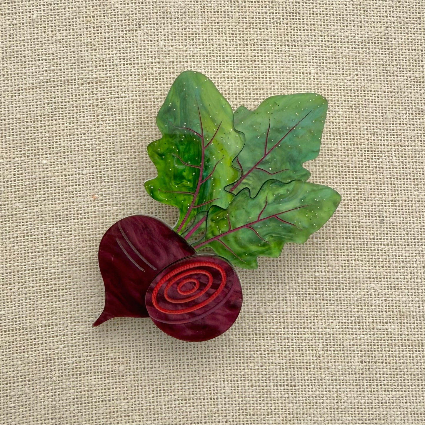 Acrylic brooch of a beet and green leaves on a textured beige background