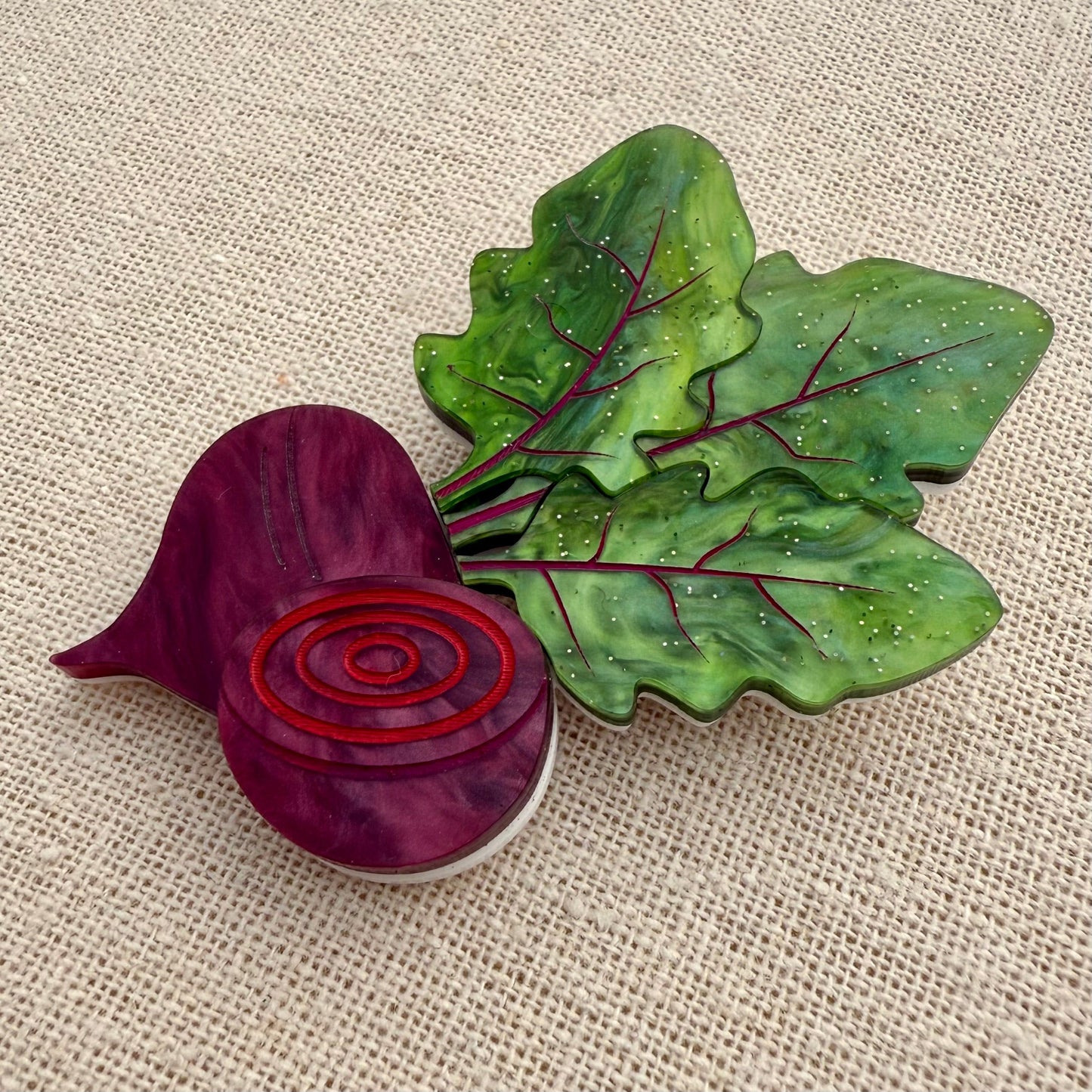 Acrylic brooch of a beet and green leaves on a textured beige
