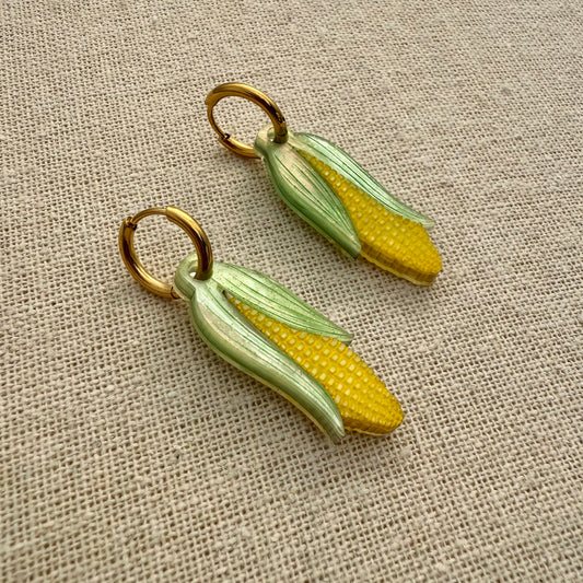 Corn-shaped earrings on a textured beige fabric background