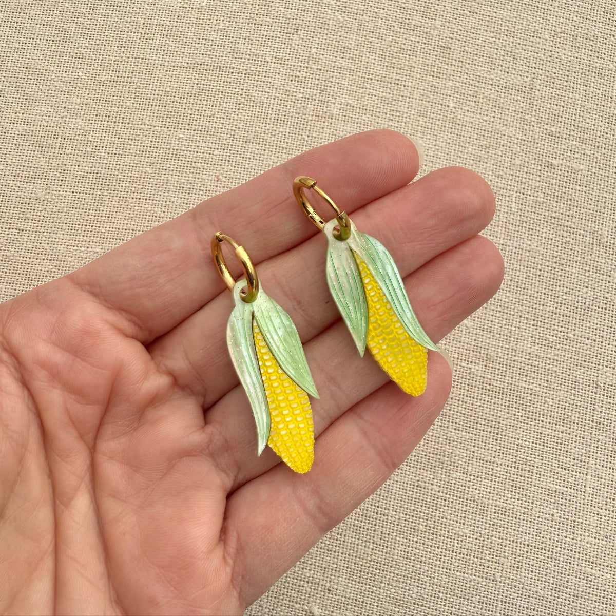 Hand holding corn-shaped earrings with a beige background