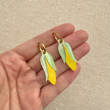 Load image into Gallery viewer, Hand holding corn-shaped earrings with a beige background
