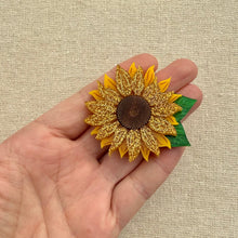 Load image into Gallery viewer, Sunflower brooch with glittery petals held in a hand against a beige background
