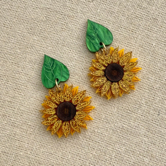 Sunflower earrings with green leaves on a textured beige background