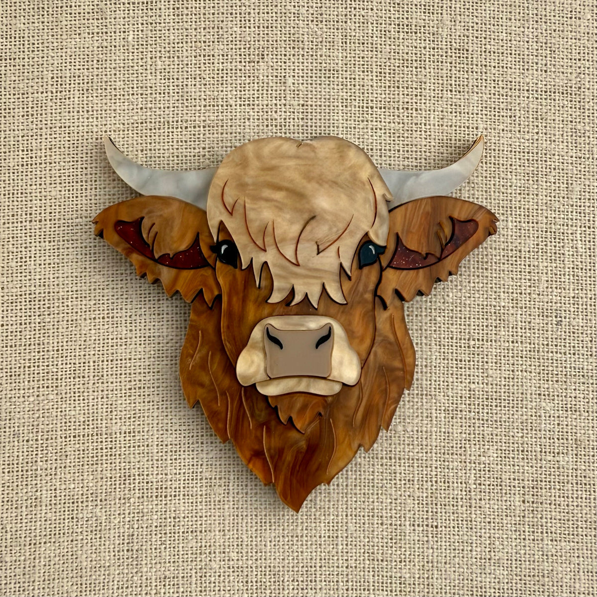 Highland cow head acrylic brooch on a textured beige background