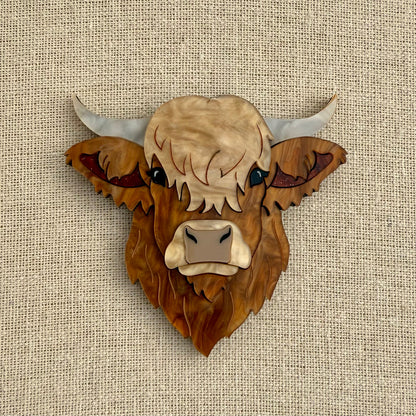 Highland cow head acrylic brooch on a textured beige background