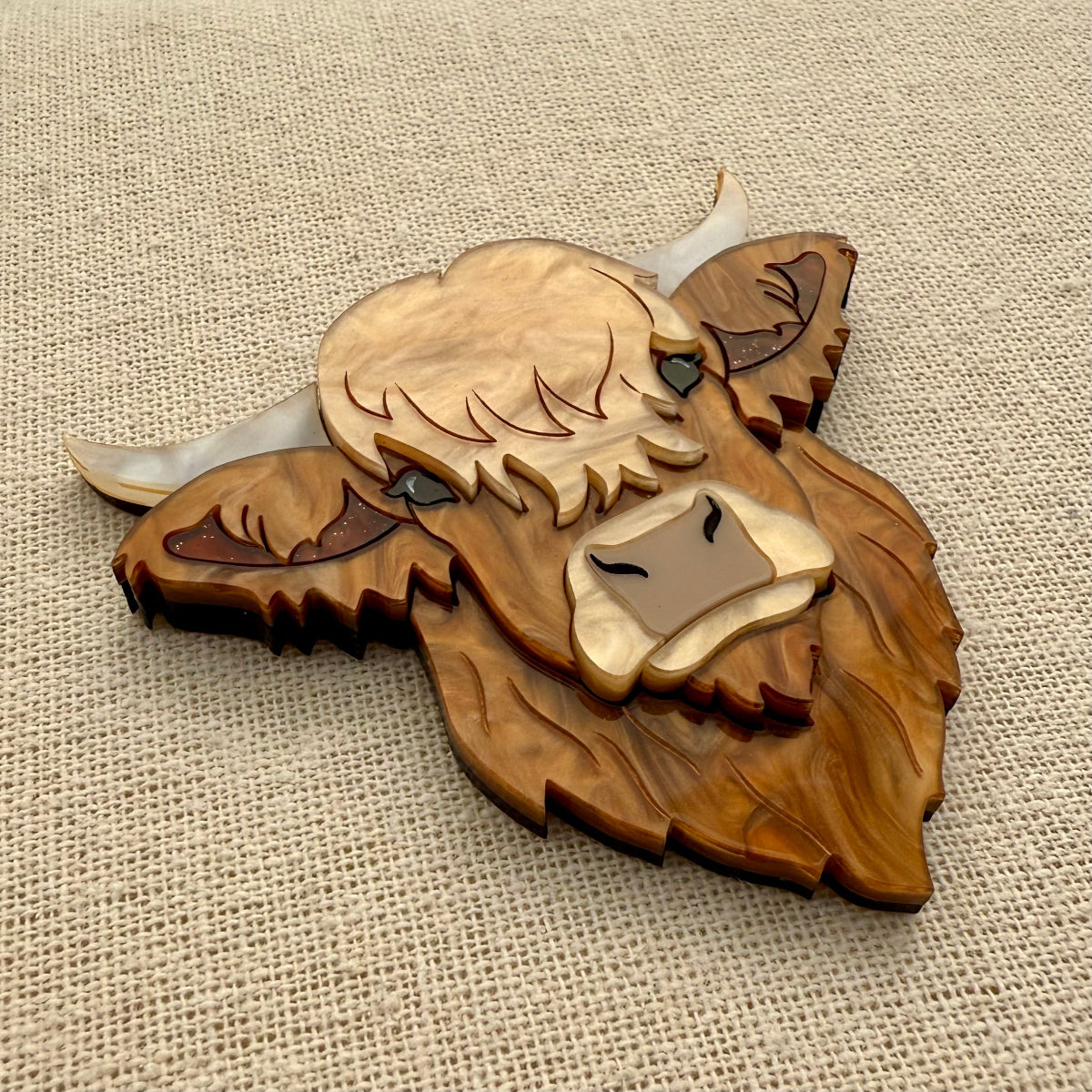 Highland cow head acrylic brooch on a textured beige background