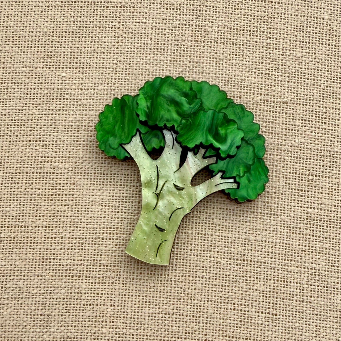 Green broccoli-shaped brooch on a beige fabric background