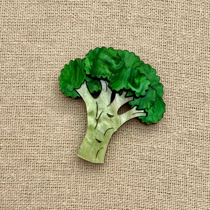 Green broccoli-shaped brooch on a beige fabric background
