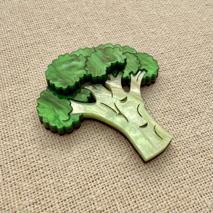 Green broccoli-shaped brooch on a beige fabric background