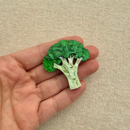 Green broccoli-shaped brooch being held on a beige fabric background