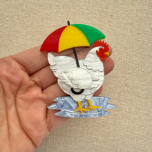 Load image into Gallery viewer, White chicken with a colorful umbrella held in a hand against a beige background
