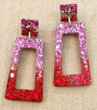 Load image into Gallery viewer, Pair of glittery red and pink earrings on a beige background

