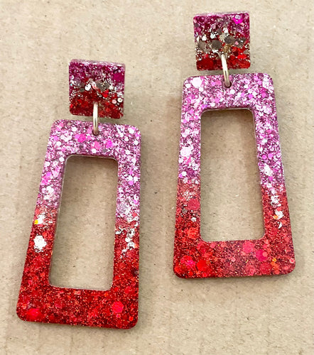 Pair of glittery red and pink earrings on a beige background