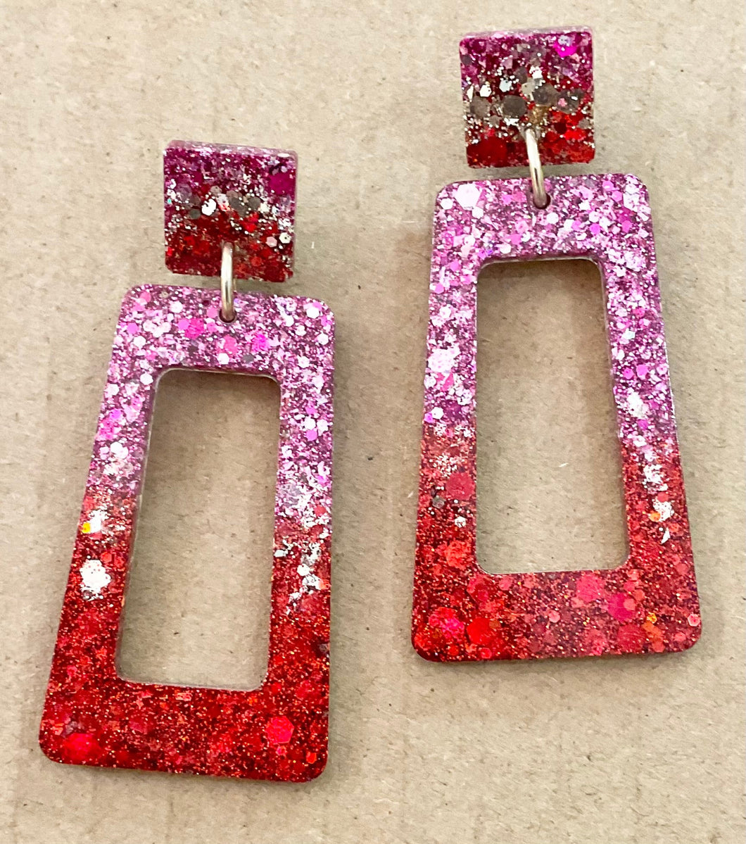 Pair of glittery red and pink earrings on a beige background